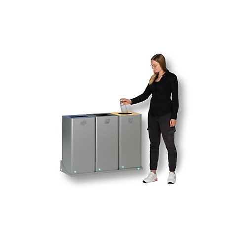 Vrouw die glas in een afvalbak gooit. Drie grijze bakken met gekleurde deksels: blauw, zwart en geel.