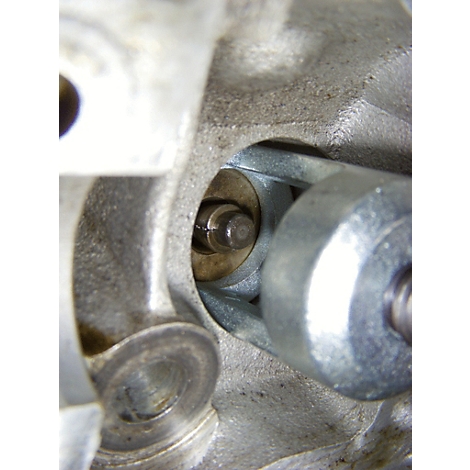 Nahaufnahme eines Motorenteils: Ein Bolzen in einer Aussparung, umgeben von grauem Metall. Ein Schraubenschlüssel liegt rechts.