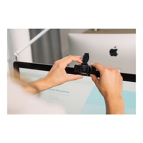 Person befestigt Webcam an Monitor. Im Hintergrund ist ein Apple Monitor mit Apfel-Logo zu sehen.