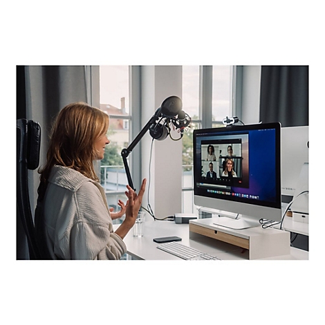 Frau im Homeoffice fÃ¼hrt Videokonferenz. Mikrofon, Monitor mit Teilnehmern, helle Umgebung.