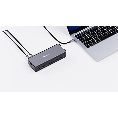 Graue Dockingstation mit verschiedenen Anschlüssen, verbunden mit einem Laptop auf weißem Hintergrund.