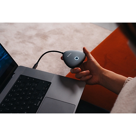 Person hält einen dreieckigen, grauen Barco ClickShare Button mit leuchtendem Ring an einem Laptop.