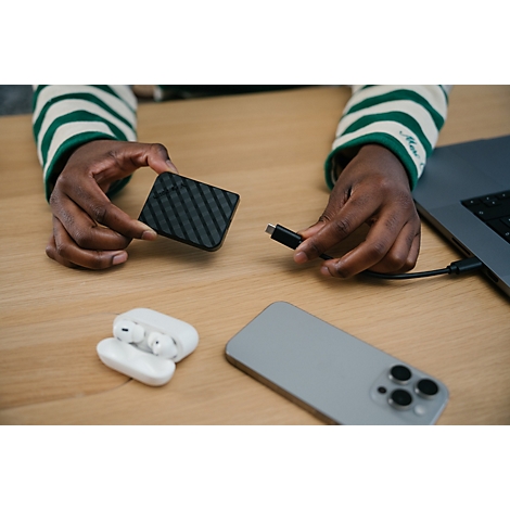 Person verbindet eine externe SSD mit einem Laptop an einem Schreibtisch mit Smartphone und Kopfhörern.