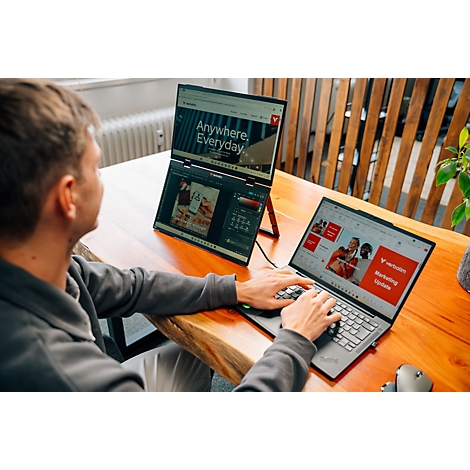 Person arbeitet an einem Laptop mit angeschlossenem zweiten Bildschirm auf einem Holztisch.
