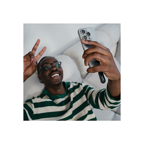 Ein Mann mit Brille macht ein Selfie. Er zeigt das Victory-Zeichen und lächelt. Er hält ein Handy in der Hand.