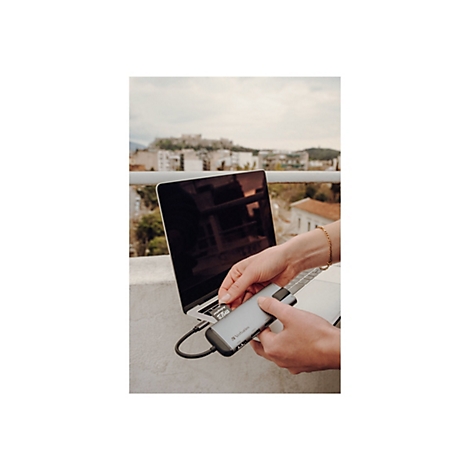 Une personne insère une carte SD dans un adaptateur USB-C tout en travaillant sur un ordinateur portable. Des bâtiments et une ville sont visibles en arrière-plan.