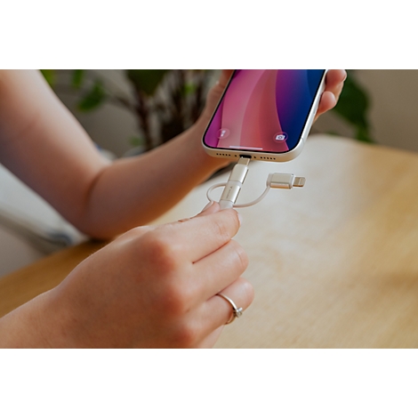 Person steckt einen weißen Ladeadapter in den Anschluss eines hellen Smartphones.