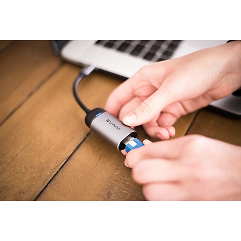 Hände stecken einen blauen USB-Stick in einen grauen Verbatim USB-C-Hub, der an einem Laptop angeschlossen ist.