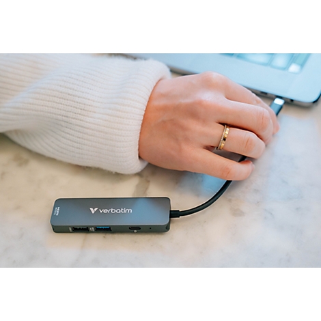 Eine Hand schließt einen grauen Verbatim USB-C-Hub an einen Laptop an.