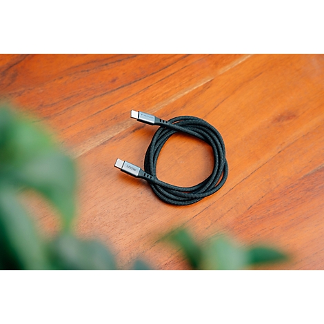 Ein aufgerolltes, schwarzes USB-C-Kabel mit Textilummantelung auf einem hölzernen Untergrund.