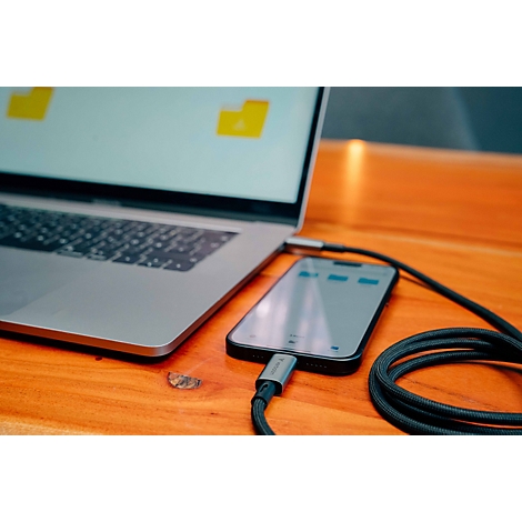 Laptop und Smartphone sind über ein schwarzes Kabel auf einem Holztisch miteinander verbunden.