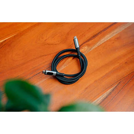 Ein schwarzes USB-C-Kabel mit grauen Metallsteckern liegt auf einem hölzernen Untergrund.
