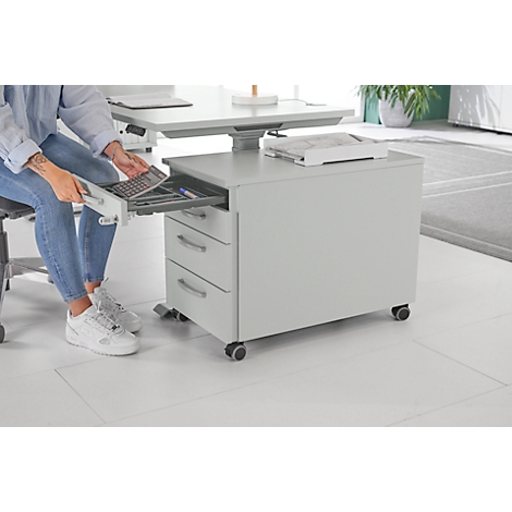 Persoon opent een lade van een rolcontainer. Pennen en een toetsenbord liggen in de container.