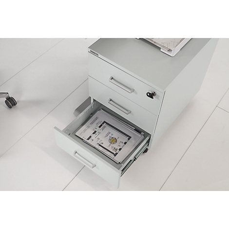 Lichtgrijze roldeurkast, één lade open. Er liggen papieren met tekeningen in.