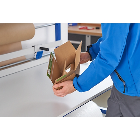 Person hält offene Kartonverpackung an Packtisch. In der Nähe befindet sich ein Kartonrollenhalter.
