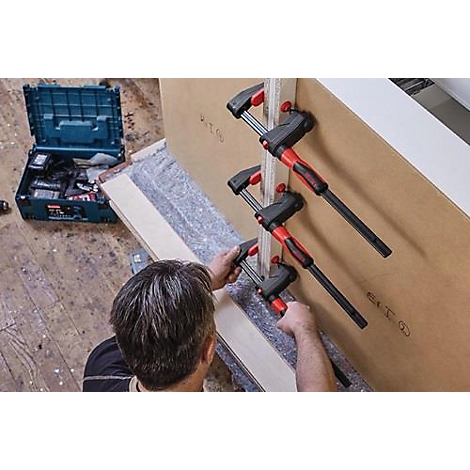 Man gebruikt klemmen om twee houten planken vast te zetten. Gereedschapskist op de achtergrond.
