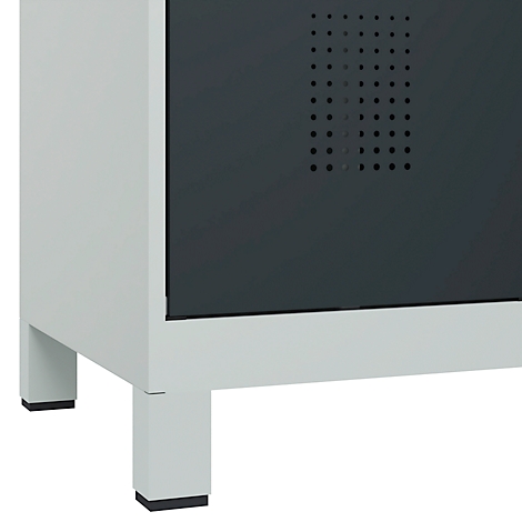 Gros plan d'une armoire grise reposant sur quatre pieds carrés. Des trous de ventilation sont visibles sur la porte sombre.