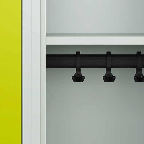 Gros plan de l'intérieur d'une armoire avec une barre noire et des crochets pour vêtements. Une porte jaune à gauche. Derrière, une construction blanche.
