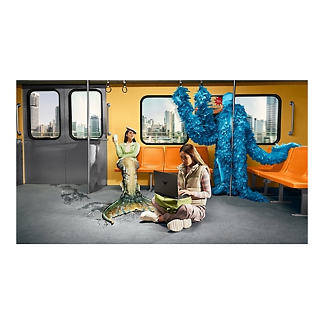 Eine Frau arbeitet mit einem Laptop in einer U-Bahn. Neben ihr sitzt eine Meerjungfrau, dahinter ein blaues Wesen mit Federn. Im Hintergrund eine Skyline.