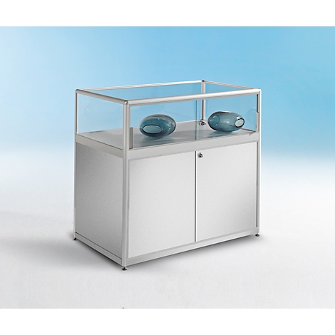 Une table vitrifiée élégante en aluminium avec un dessus en verre. À l'intérieur, il y a deux boules de verre ovales bleues. La table a un compartiment fermé blanc en dessous et repose sur quatre pieds transparents. Arrière-plan en bleu doux.