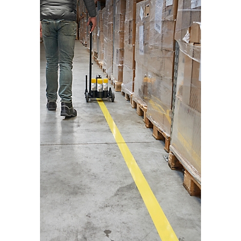 Persoon met een gele lijnenmarkeermachine in een magazijn. Gele lijn op betonnen vloer. Pallets met verpakte dozen.