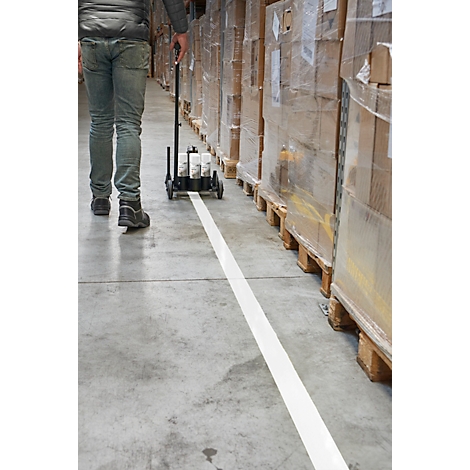 Persoon die een markeertrolley trekt en een witte lijn op de betonnen vloer trekt, in het magazijn. Pallets met goederen staan op de achtergrond.