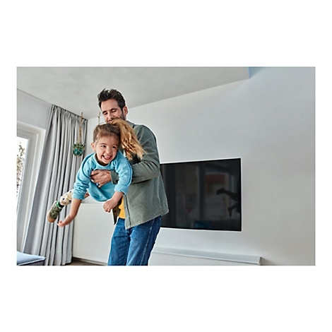 Ein Mann hält ein lachendes Kind in der Luft; Freude im hellen Wohnzimmer.