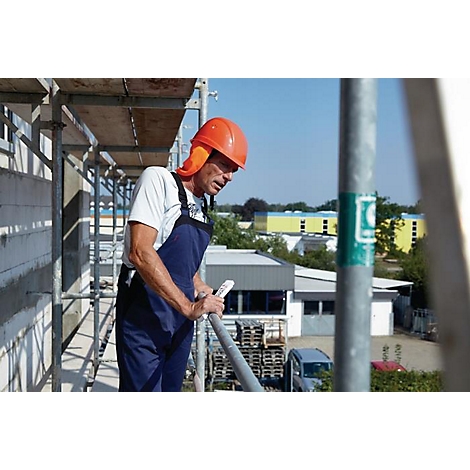 Un ouvrier du bâtiment portant un casque sur un échafaudage, regardant le chantier.