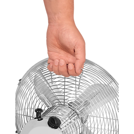 Close-up van een hand die een ventilatorhandvat vasthoudt. Het metalen rooster en de bladen zijn goed zichtbaar.