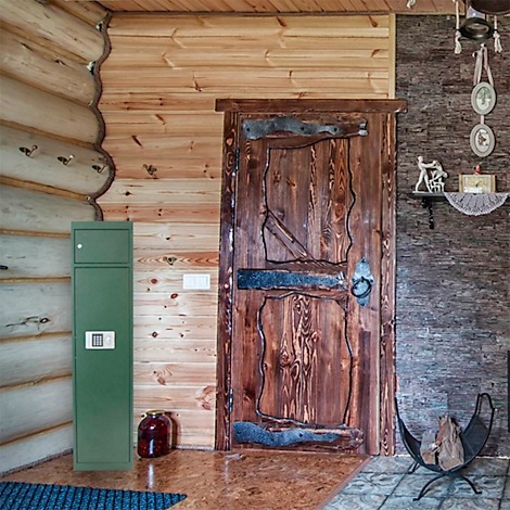 Ein grüner Waffenschrank mit Zahlenschloss steht in einem rustikalen Raum vor einer Holzwand.
