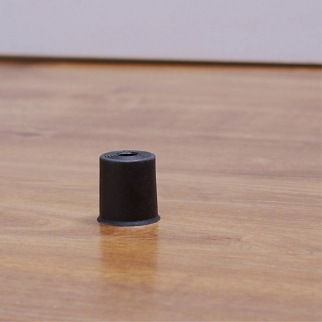 Schwarze, zylindrische Abdeckung für einen Möbelbein, auf hellem Holzboden. Das Objekt ist in der Mitte platziert.