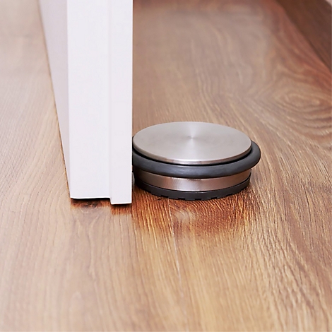 Een metalen en rubberen deurstopper houdt een deur open op een houten vloer.