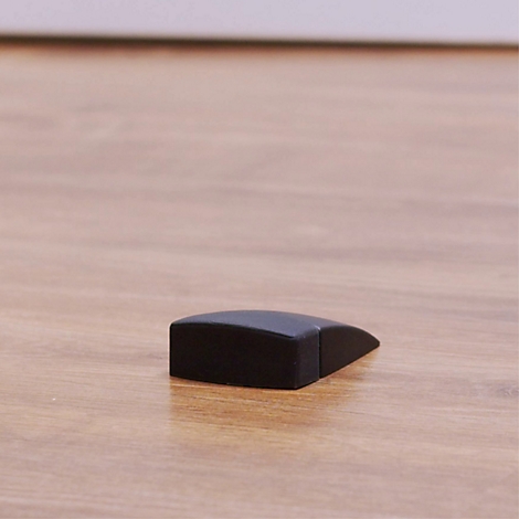 Ein schwarzer Türstopper aus Holz liegt auf einem hellbraunen Holzboden. Der Stopper hat eine rechteckige Form mit einer abgeschrägten Seite.