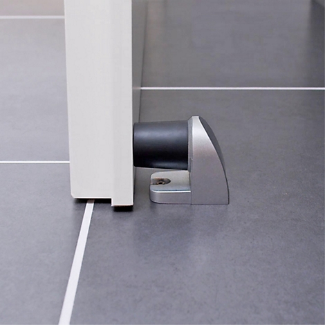 Een deurstoppers bevestigd aan een witte deur. Op grijze vloer. Het licht komt van bovenaf binnen.