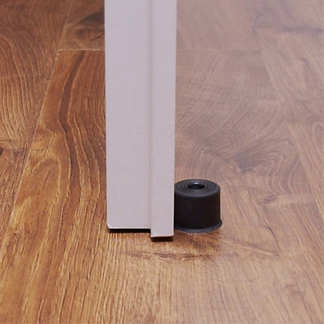 Zwarte deurstopper die een witte deur tegenhoudt die op een houten vloer staat.