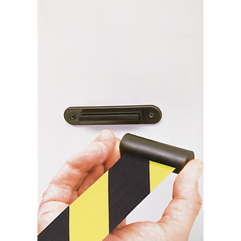 Person holding yellow and black warning tape. A dark holder is attached above on a white wall.