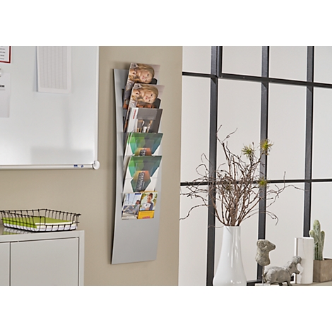 Grey wall newspaper with brochures, next to it window, flower vase and decoration.