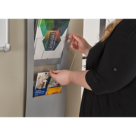 A woman opens a brochure compartment. Brochures with prints can be seen inside. The woman is wearing a black top.