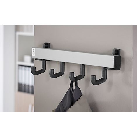 Wandgarderobe met vier haken, waaraan een jas hangt. Daarachter een grijze muur en een plank.