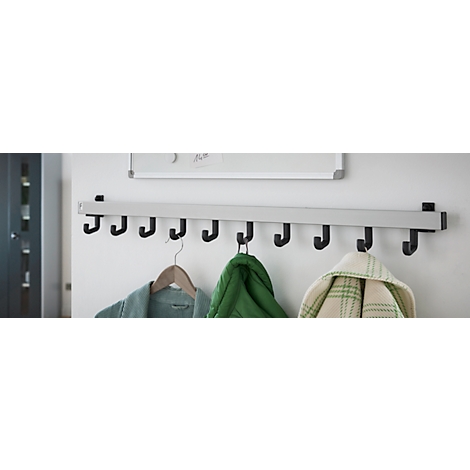 Garderobenleiste mit schwarzen Haken an weißer Wand. Kleidung hängt an einigen Haken.