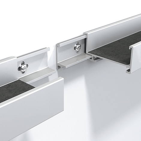 Detailaufnahme von silberfarbenen Aluminiumprofilen, die an einer weißen Wand befestigt sind. Schwarzes Filz ist sichtbar.
