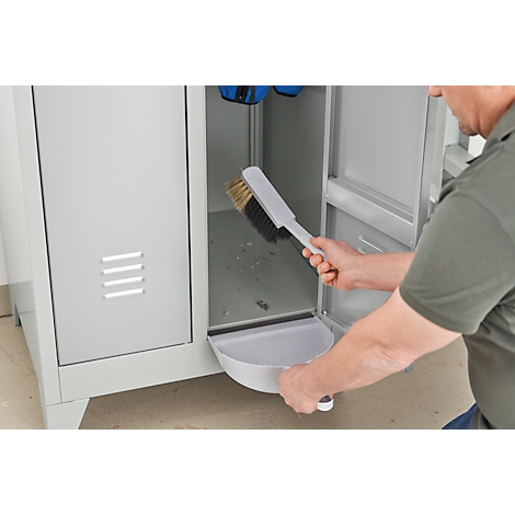 A person cleaning a gray cabinet with a dustpan and brush.