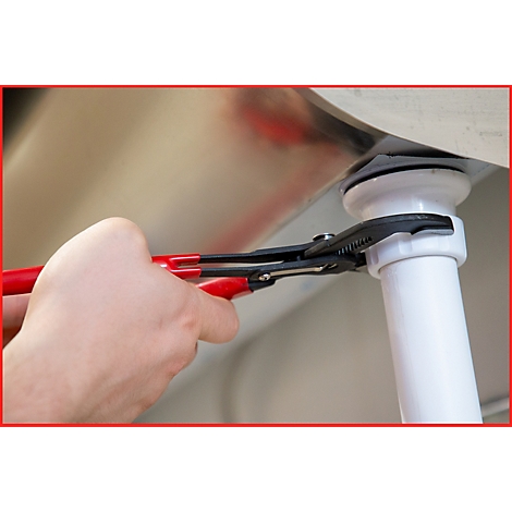 Eine Hand mit einer roten und schwarzen Zange repariert einen weißen Rohrabfluss unter einem Waschbecken.