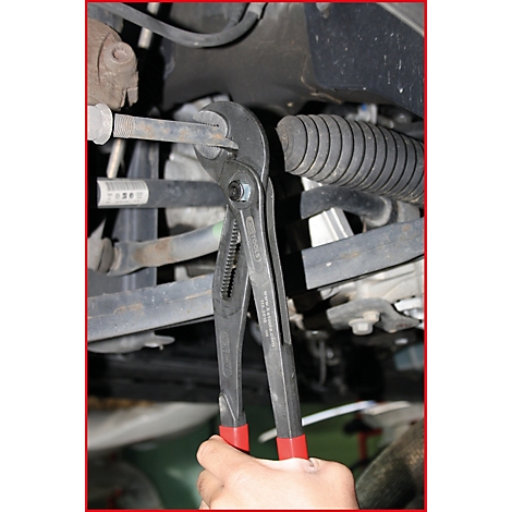 Eine Person hält eine Zange an einem Autoteil. Roter Griff, graue Zange, Autoteile im Hintergrund.
