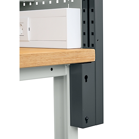 Nahaufnahme einer Werkbank mit einer Holzplatte, einer weißen Box und einem grauen Metallrahmen. An der Seite sind Schlüsselform-Ausschnitte.
