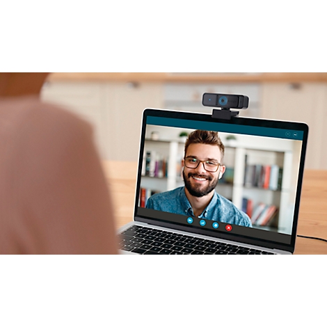 Gros plan d'un ordinateur portable avec une visioconférence. Un homme souriant à l'écran, une personne au premier plan, une webcam en haut.