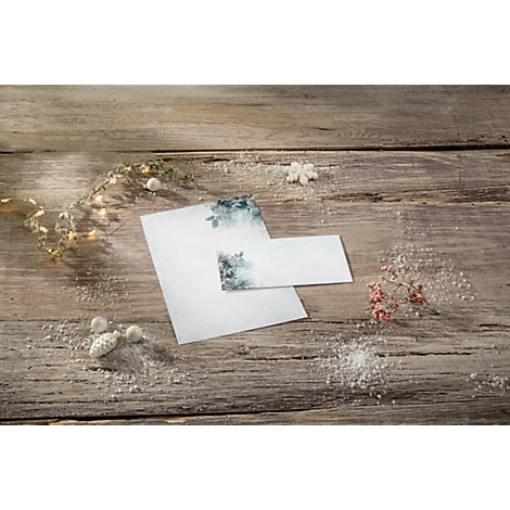 Papier mit floralem Muster liegt auf rustikalem Holz. Dekoration: Blüten, Eisblumen, Lichterkette.