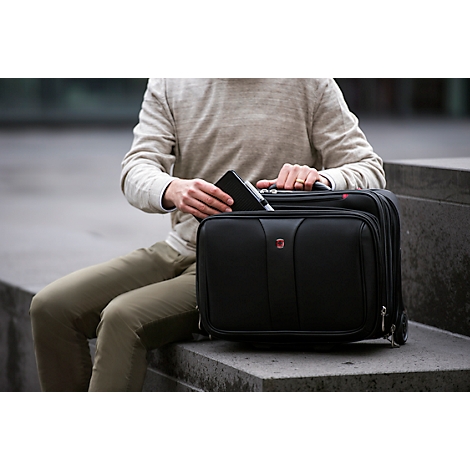 Man puts smartphone into black trolley, sitting outdoors.