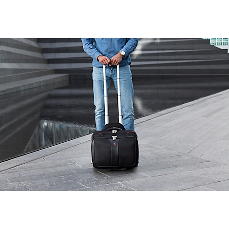 Man standing with a rolling suitcase. He is wearing jeans and a denim shirt.