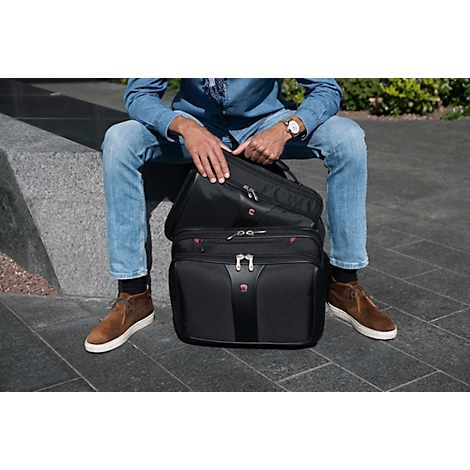 Man sitting with open black travel bag. He is wearing jeans, a denim jacket, brown shoes and a wristwatch.
